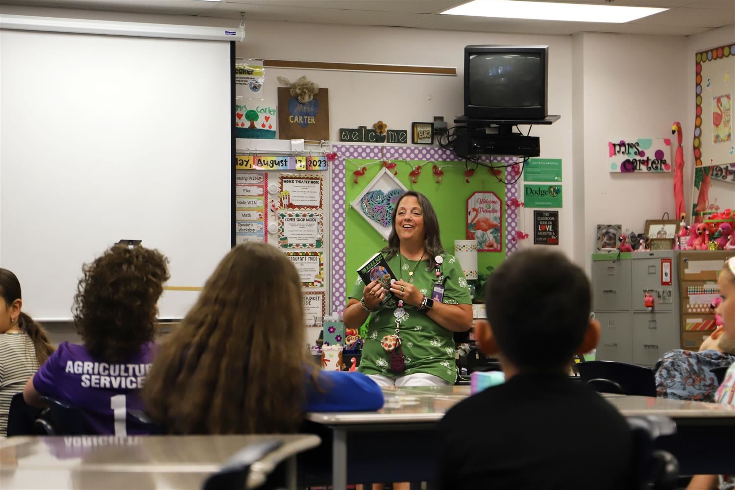 Mrs. Michelle Carter smiling and holding a book in front of her class of 5th Grade Dodge Elementary students.